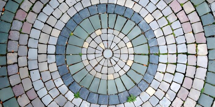 An aerial view shows a beautiful circular pattern made from grey and colored cobblestones with some green grass growing between them photo