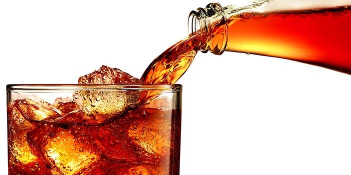 A refreshing brown carbonated beverage pours from a bottle into a glass filled with ice cubes creating a dynamic effect photo