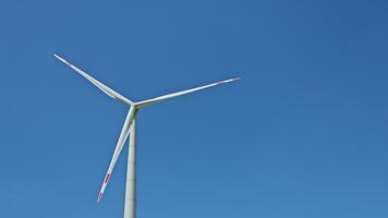 large wind turbine against a blue sky. Windmills generate energy when they are turned by the wind while standing in a field. The turbine has three blades that are attached to a pole video