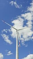 vind turbin mot en blå himmel. väderkvarnar generera energi när de är vände sig förbi de vind medan stående i en fält. de turbin har tre blad den där är bifogad till en Pol video