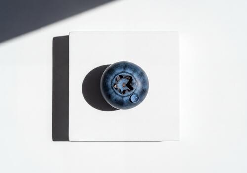 Detailed View of a Single Fresh Blueberry with Water Droplet on White Cube photo