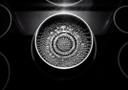 Monochrome overhead view of boiling water with many bubbles in a metal pot on an electric cooktop photo