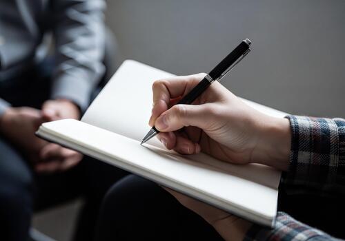 Close up of a hand writing notes with a pen in a notebook during a discussion or interview session photo