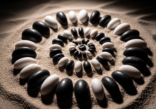 Black and White Oval Stones Arranged in an Elegant Spiral Pattern on Textured Sand with Dramatic Lighting photo