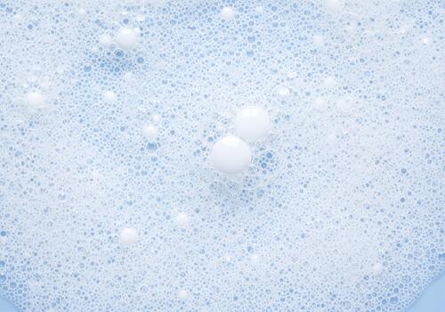 Close up view of white soap foam and bubbles on a light blue background surface photo