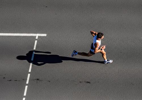 Fit Man Running on Asphalt Road with Prominent Shadow from High Angle View on Sunny Day photo