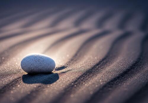 Smooth grey stone resting on textured sand with sunlit wave patterns and soft bokeh glow photo