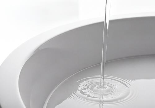 Clear water stream pouring into a white basin creating ripples photo