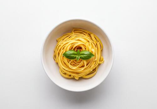 Fresh Raw Tagliatelle Pasta Nest in White Bowl with a Vibrant Basil Leaf on a Clean Background photo