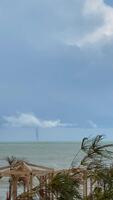 Waterspouts form over ocean under stormy clouds with palm trees swaying, suitable as background video