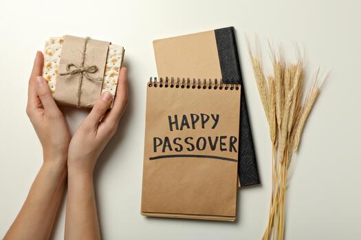 Matzo in hands, spikelets and notepad with text on white background, top view photo