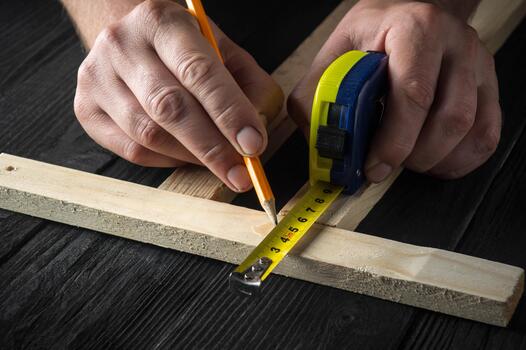 Woodworker makes pencil marks on a block of wood. Hands of the master close-up at work. Working environment in a carpentry workshop. photo