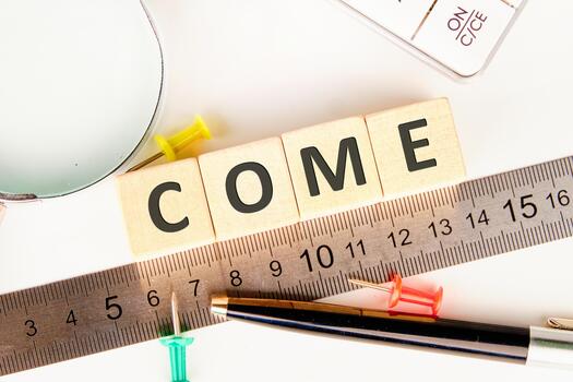 A bright workspace features wooden blocks spelling the word come. A ruler lies nearby along with colorful push pins and a magnifying glass, creating an inviting atmosphere for creativity photo