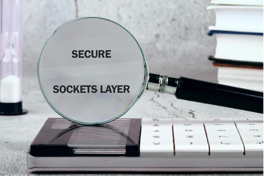 A magnifying glass reveals the phrase secure sockets layer on a calculator while books are stacked in the background, highlighting the importance of online security photo