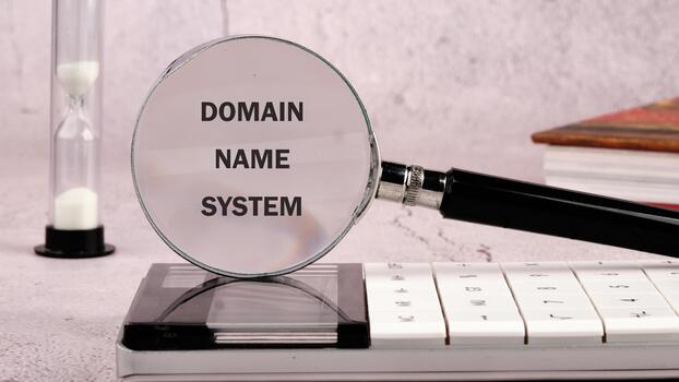 A magnifying glass highlights the term Domain Name System placed on a modern calculator, alongside an hourglass, symbolizing time and technology in a studied environment photo