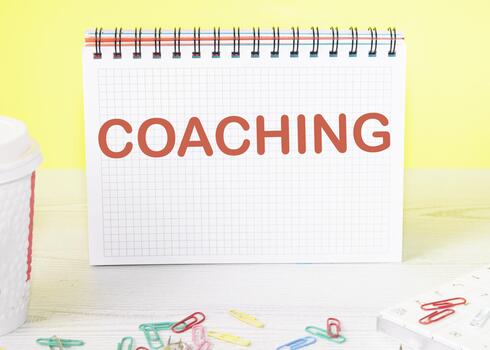 COACHING the word is written on a blank sheet in a notebook standing on a table on a yellow background photo