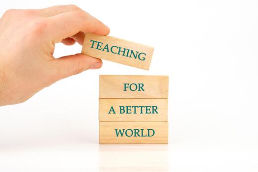 A hand carefully places a block that spells Teaching atop a tower of wooden blocks marked with the phrase For a Better World, emphasizing the importance of education in shaping the future photo
