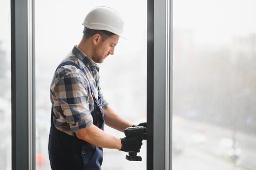 Construction worker installing window frame using cordless drill in building photo