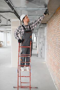 Builder working on ventilation system using ladder in building under construction photo