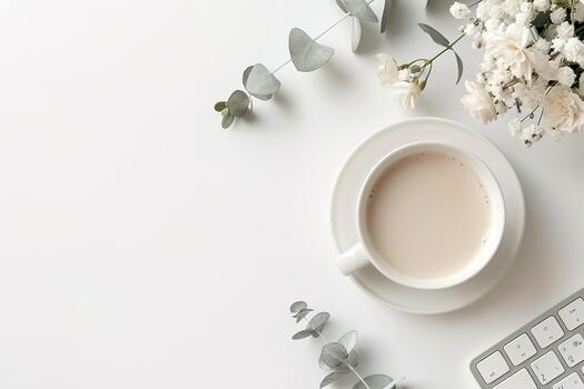 A top view of a simple white desk scene features the upper half of a keyboard. A cup of coffee sits beside a small bouquet of flowers and greenery, creating a calm atmosphere photo