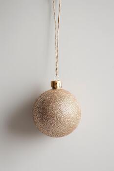 un reluciente oro Brillantina ornamento cuelga desde un sencillo cuerda en contra un ligero fondo, Perfecto para agregando festivo animar a ninguna fiesta ajuste foto