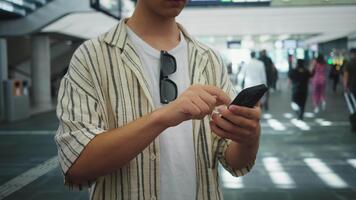 viajante Verificações trem agendar, viajante usa telefone para viagem informação no meio ocupado ambiente, pessoa interage com Móvel dispositivo enquanto navegação lotado estação atmosfera durante comutar video