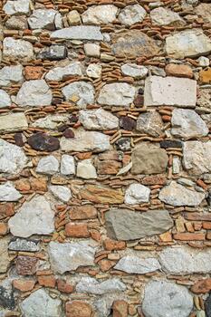 A close-up of a rustic stone wall with uneven natural stone and brick elements. Ideal as a background or pattern for design, architecture, and creative projects. photo