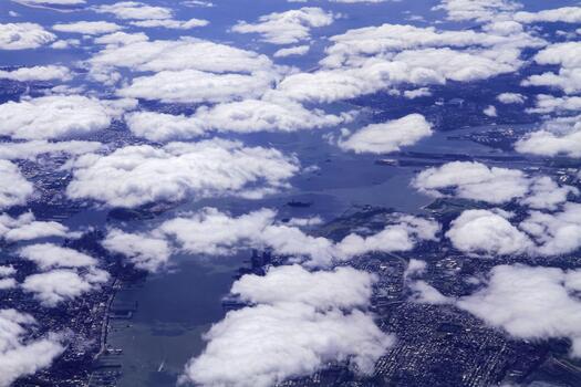 A panoramic photograph of New York City, partially obscured by clouds, taken from an airplane window. The image features the coastline, cityscape, waterways, and cloud formations photo