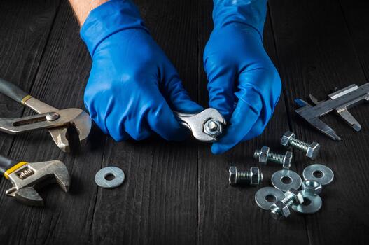The master tightens the nut with a wrench on the bolt closeup. Working environment on a table in a workshop with tools. photo