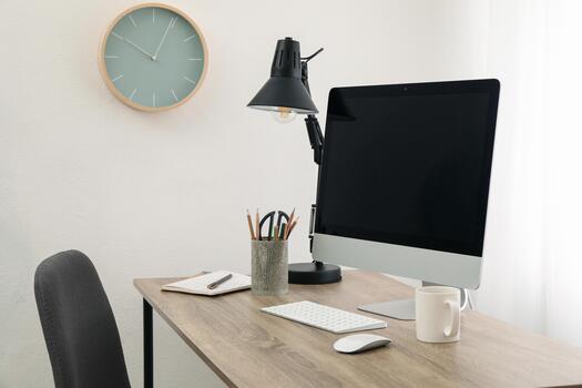 A desk with a computer monitor, a mouse, a keyboard, a clock and a cup of photo
