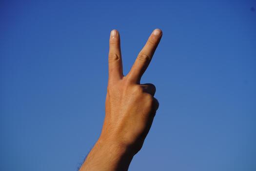 Hand gesture symbolizing peace against a clear blue sky showcasing unity, hope, and positivity in a vibrant and serene setting without distractions photo