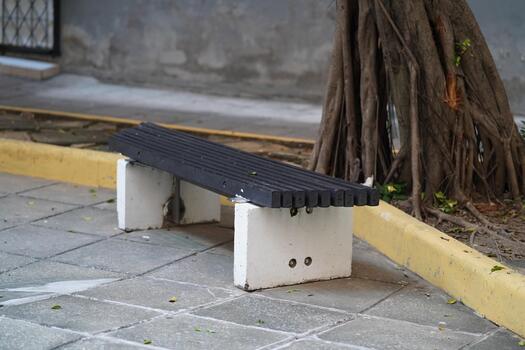 Minimalist Urban Bench in Public Space Surrounded by Nature with Tree and Pavement, Offering a Peaceful Spot for Relaxation and Reflection photo