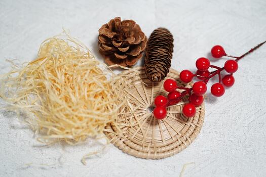 Natural elements featuring pine cones, red berries, wicker basket, and straw on textured background for decorative and artistic purposes photo