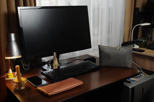 A home office workstation features a monitor, keyboard, and accessories on a dark wood desk. photo