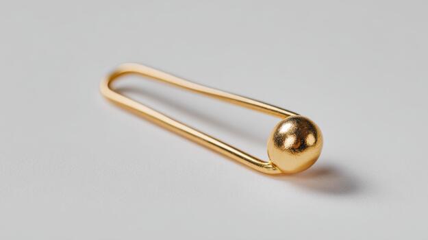 A close-up of a golden safety pin, showcasing its smooth finish and shiny surface against a minimalist background. photo
