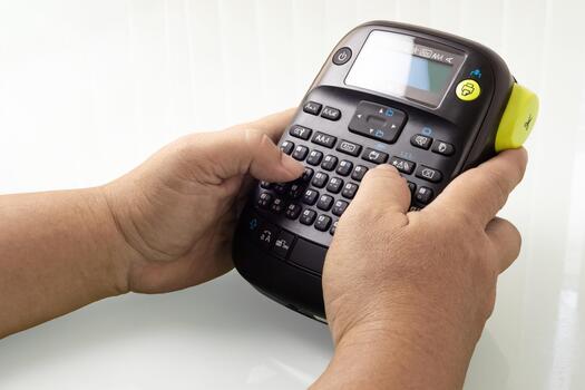 Hands hold a mobile label printer, creating custom labels isolated on white background photo