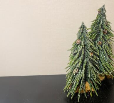 Two decorative miniature Christmas trees with pine cones placed on a dark surface against a soft neutral background. Festive holiday decor with natural green branches and rustic bases. photo