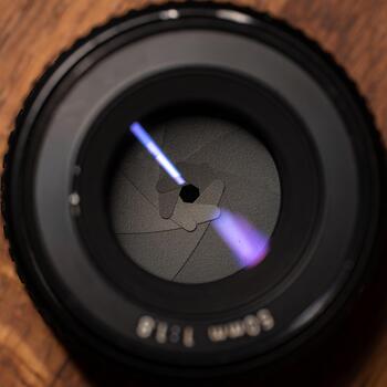 A detailed close-up of a camera lens aperture showcasing intricate patterns and textures, revealing a play of light and shadow against a wooden background, highlighting the craftsmanship photo