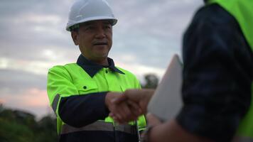 avvicinamento di un' fiducioso luogo manager o ingegnere nel un' sicurezza casco tremante mani con un' collega, simboleggiante fiducia, collaborazione, e riuscito progetto completamento su un industriale luogo a crepuscolo. video
