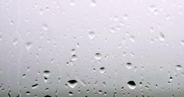 un' avvicinamento tiro di pioggia goccioline attaccamento per un' finestra Pannello, il morbido leggero di un' nuvoloso giorno filtraggio attraverso, la creazione di un' sognante, etereo umore. il dolce picchiettio di pioggia su un' finestra Pannello. video