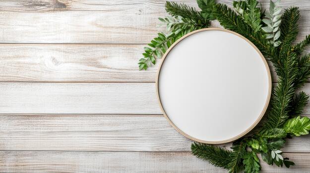 A round frame with green branches and a white oval on a wooden background photo