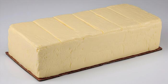 A large rectangular block of pale yellow butter is displayed on a brown cardboard sheet against a simple white background photo