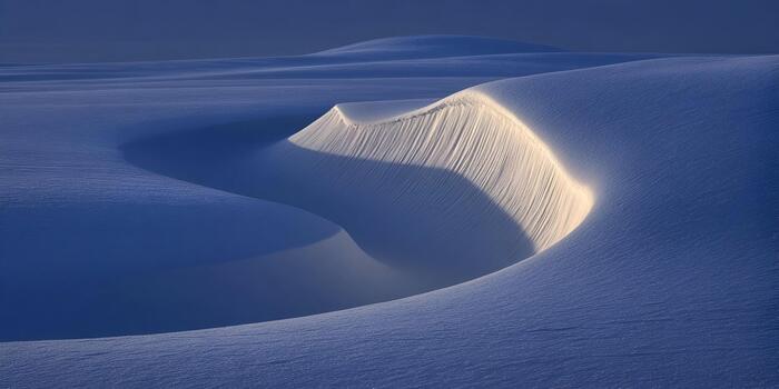 Sunlight illuminates the textured surface of a pristine blue snow dune creating abstract patterns photo