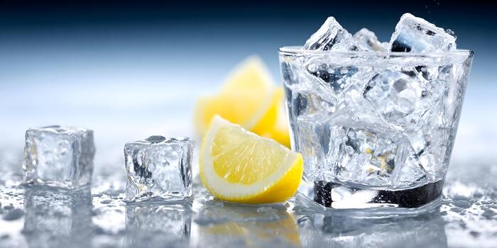un vaso desbordante con espumoso hielo cubitos y Fresco limón rebanadas se sienta en un mojado reflexivo superficie con un frio azul antecedentes foto