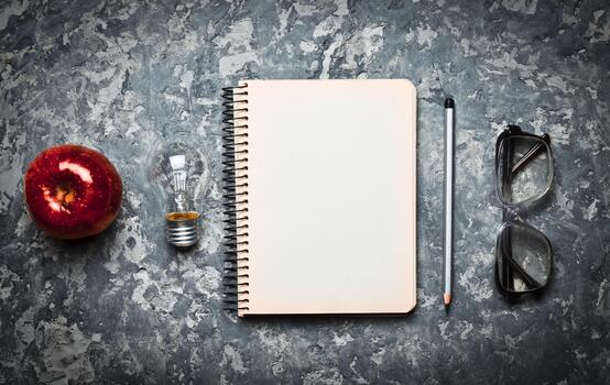 The creative workspace of the writer is inspiring to create. I have an idea. Notepad, pen, incandescent bulb, apple, glasses on a concrete table. Top view. Flat lay. photo