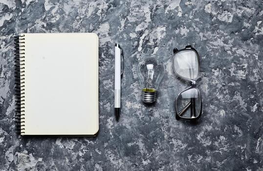 The creative workspace of the writer is inspiring to create. I have an idea. Notepad, pen, incandescent bulb, glasses on a concrete table. Top view. Flat lay. photo