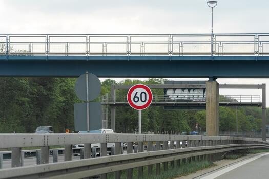 Traffic sign indicating speed limit of 60 kmh along a highway near an overpass surrounded by trees on a cloudy day photo