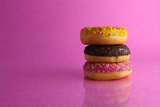 three Berliners donut pink yellow chocolate with a sprinkle on a pink background leit stack on top of each other with a place for text and with a copyspace photo