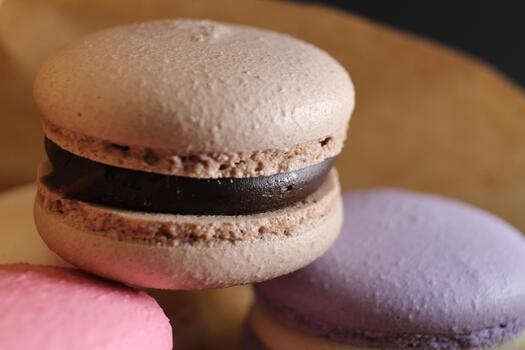 Three multi-colored macaroons lie on crafted brown paper next to lie almond sticks cinnamon and coffee on a black background with place for text and with a copyspace photo