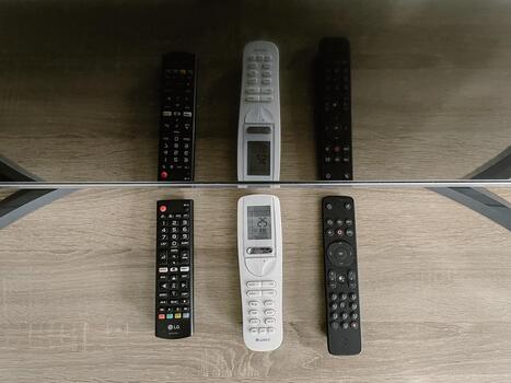 Minimalist remote lineup on wooden table with mirrored reflection, three black and white remotes arranged symmetrically under soft photo